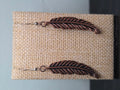 Single feather earring made from a reclaimed copper-tone charm and connector ring, shown on a wooden ruler stand measuring approximately 2.25 inches