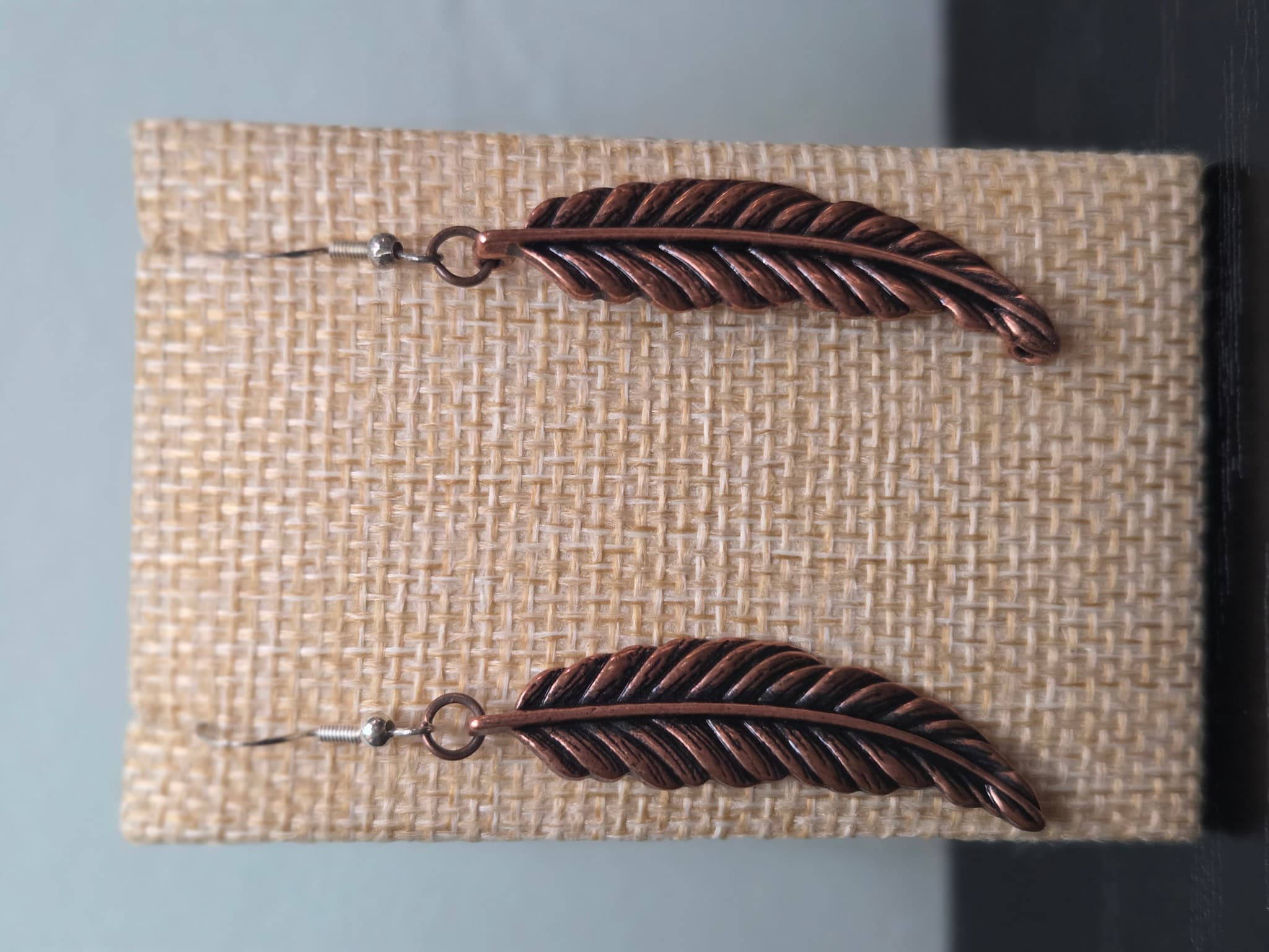 Single feather earring made from a reclaimed copper-tone charm and connector ring, shown on a wooden ruler stand measuring approximately 2.25 inches