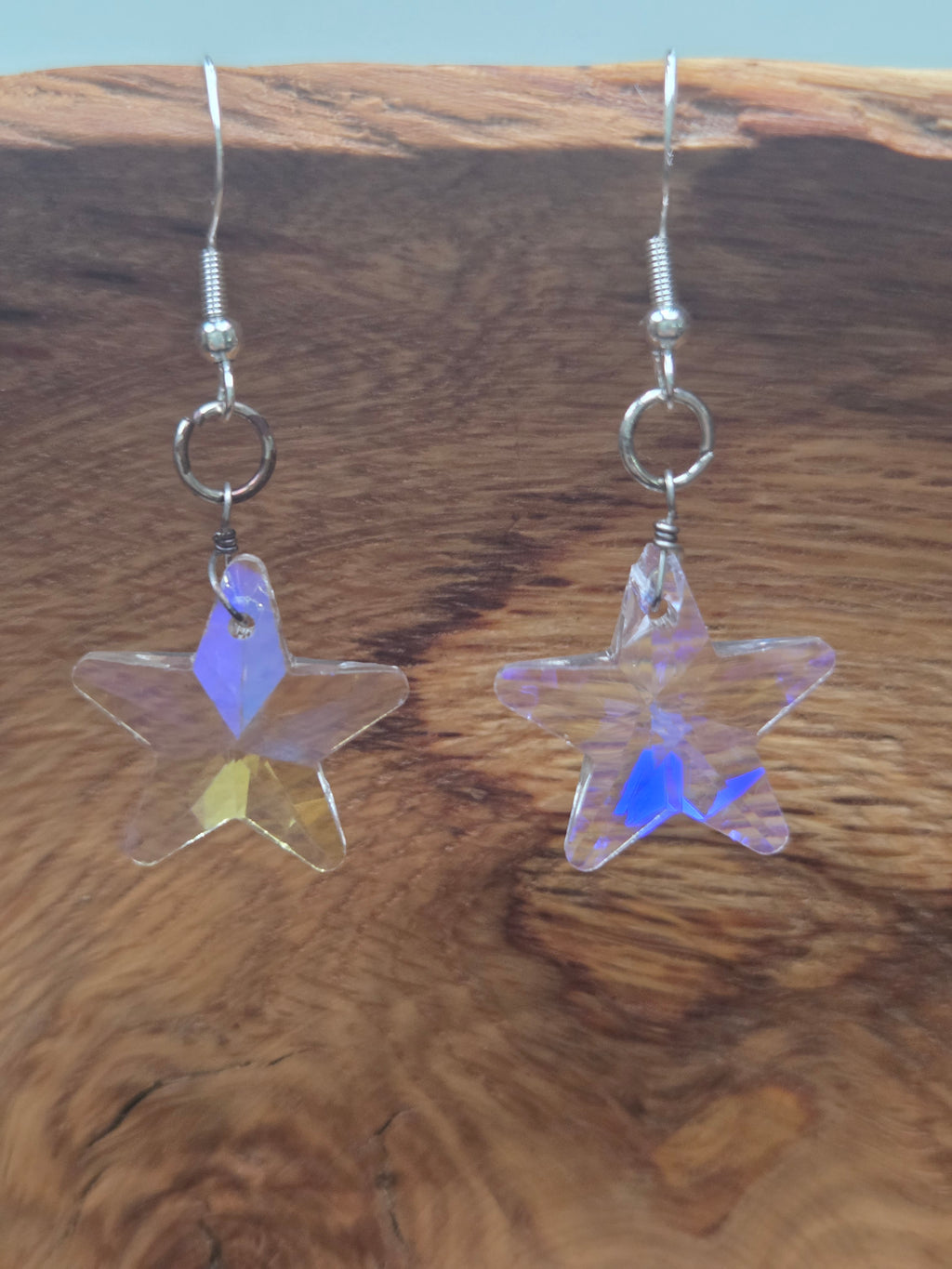 Iridescent AB crystal star earrings with aurora borealis coating showing blue and lavender flashes, displayed on rustic wood background