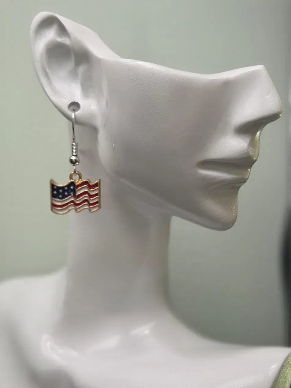 Handmade waving American flag earring on a white mannequin ear, featuring bold red and white wavy stripes with a navy blue star field and cream border in a gold-tone frame