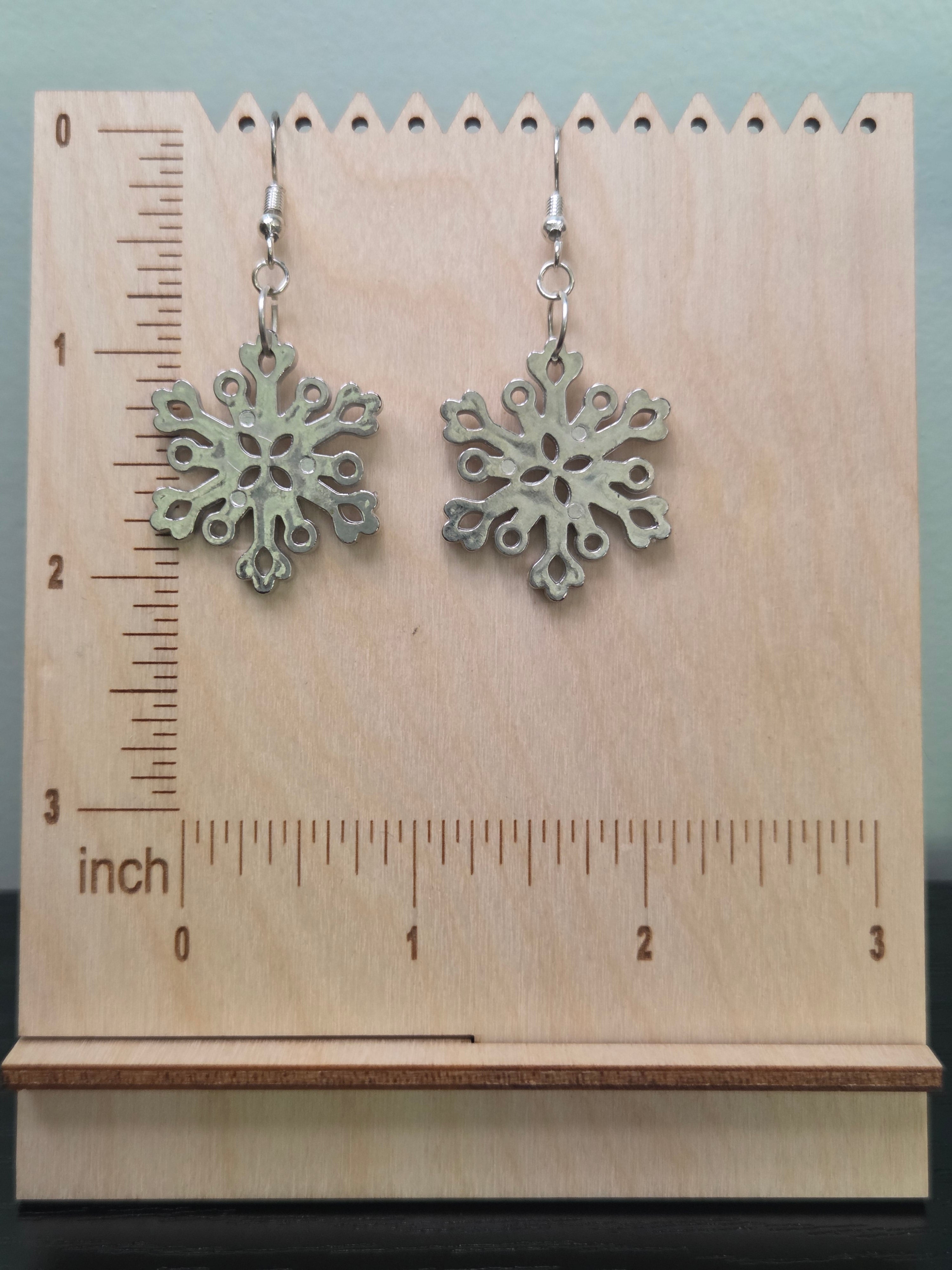 Medium acrylic snowflake drop earrings displayed on a wooden earring stand with ruler showing approximately 2 inch length
