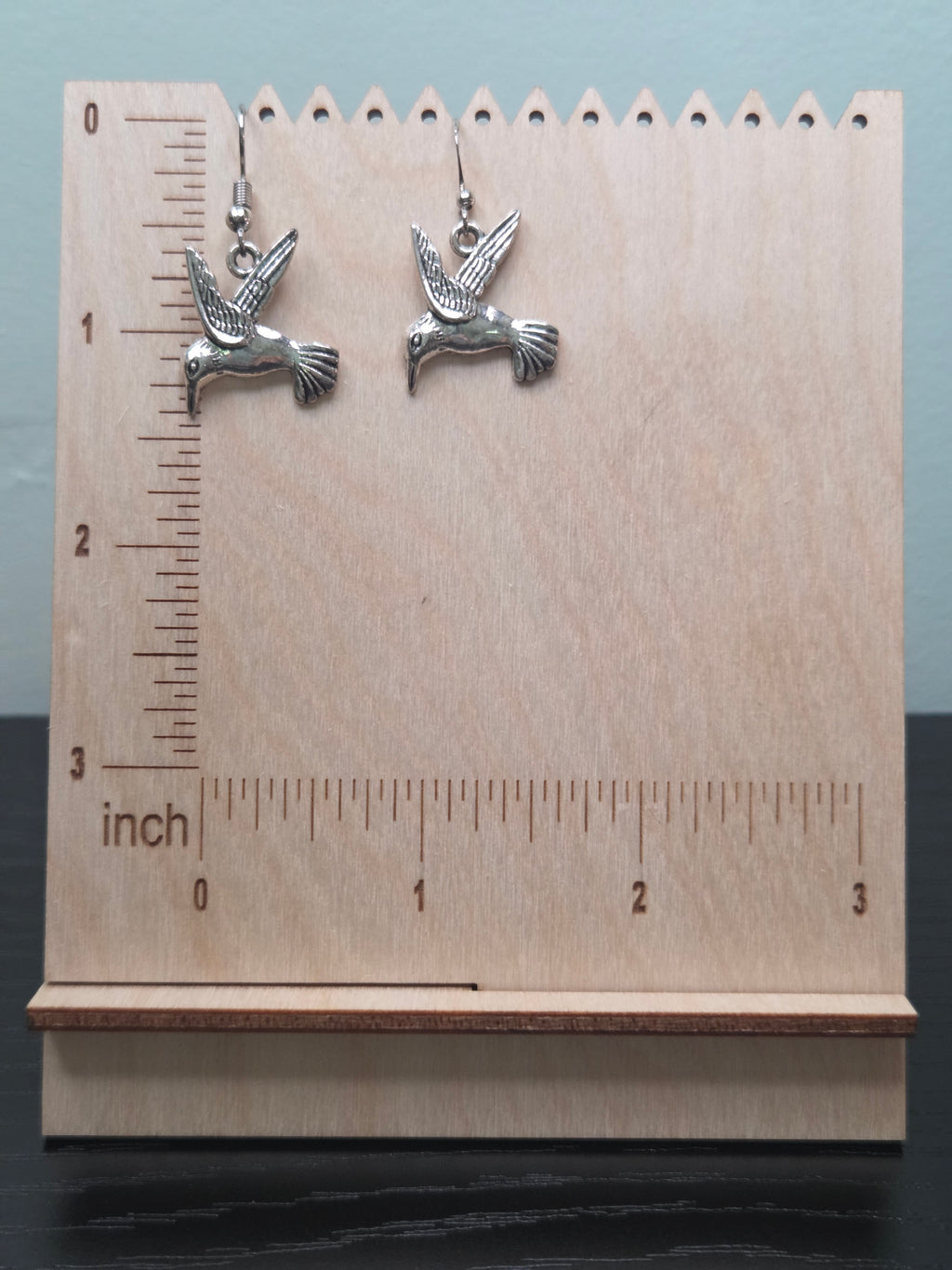Silver-tone alloy hummingbird dangle earrings against ruler showing approximately 1 inch charm length