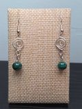 Malachite round bead earrings with silver-tone spiral charm, displayed on a wooden earring stand with ruler showing approximately 2 inch length