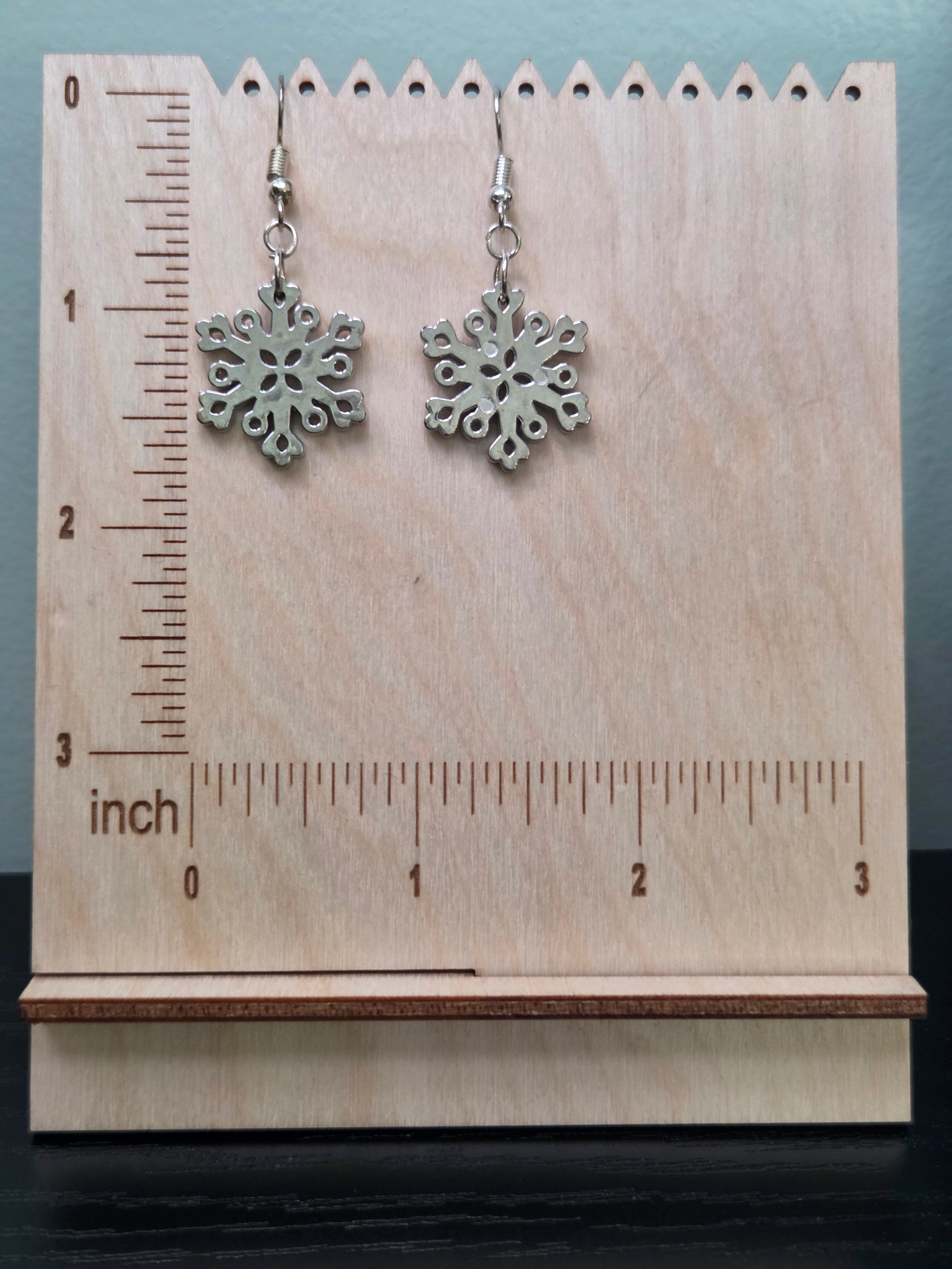 Large acrylic snowflake drop earrings displayed on a wooden earring stand with ruler showing approximately 2.25 inch length