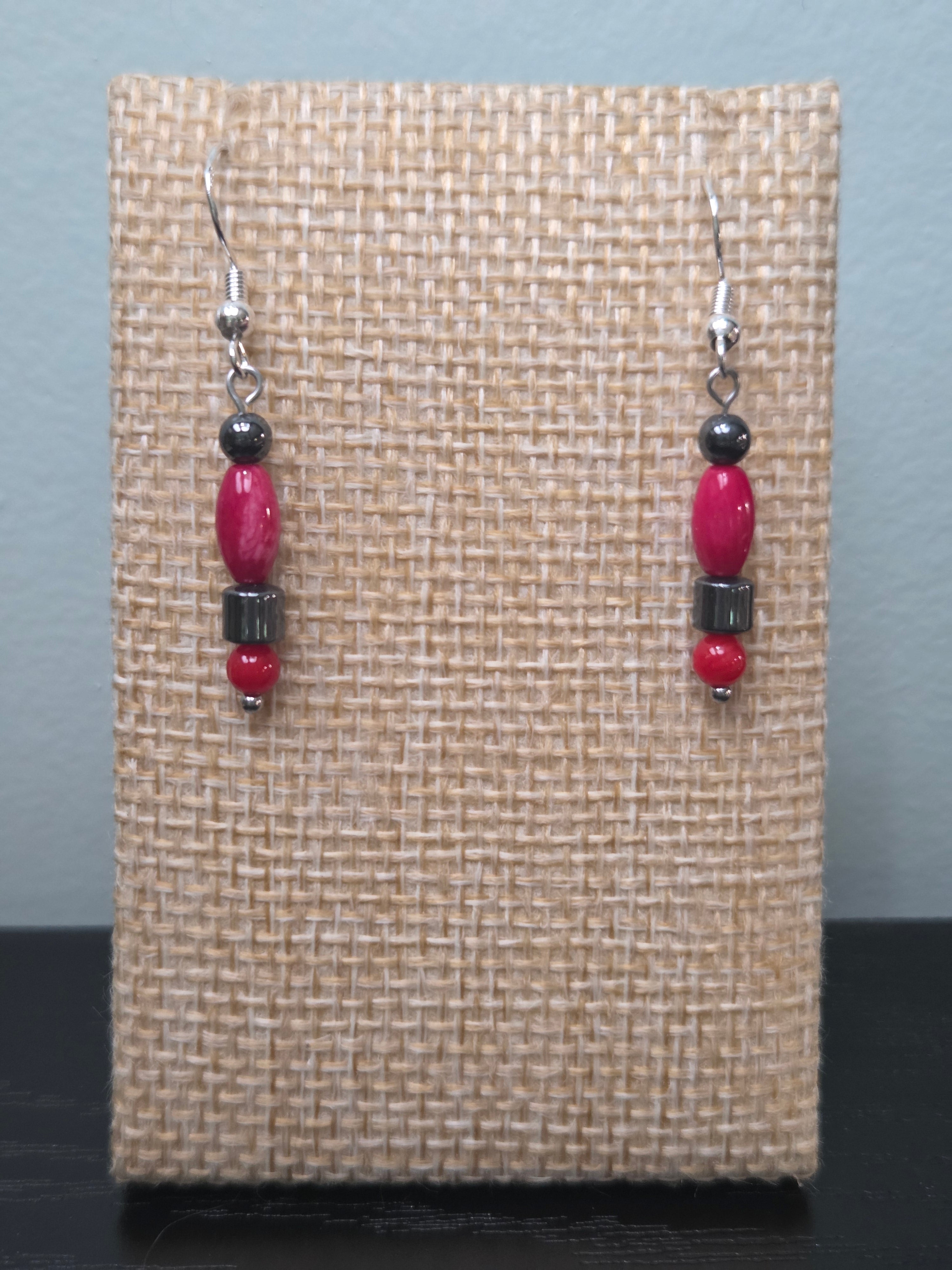 Hematite and coral stacked bead dangle earrings, shown on woven display