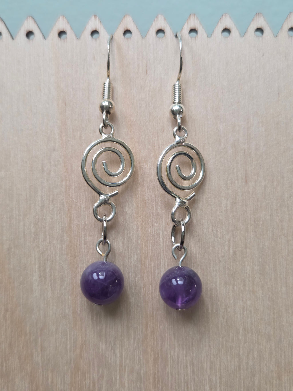 Amethyst spiral drop earrings with silver-tone spiral charm and genuine amethyst round bead, displayed on a wooden earring stand with ruler showing approximately 2 inch length