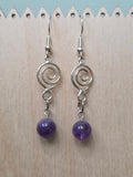 Amethyst spiral drop earrings with silver-tone spiral charm and genuine amethyst round bead, displayed on a wooden earring stand with ruler showing approximately 2 inch length
