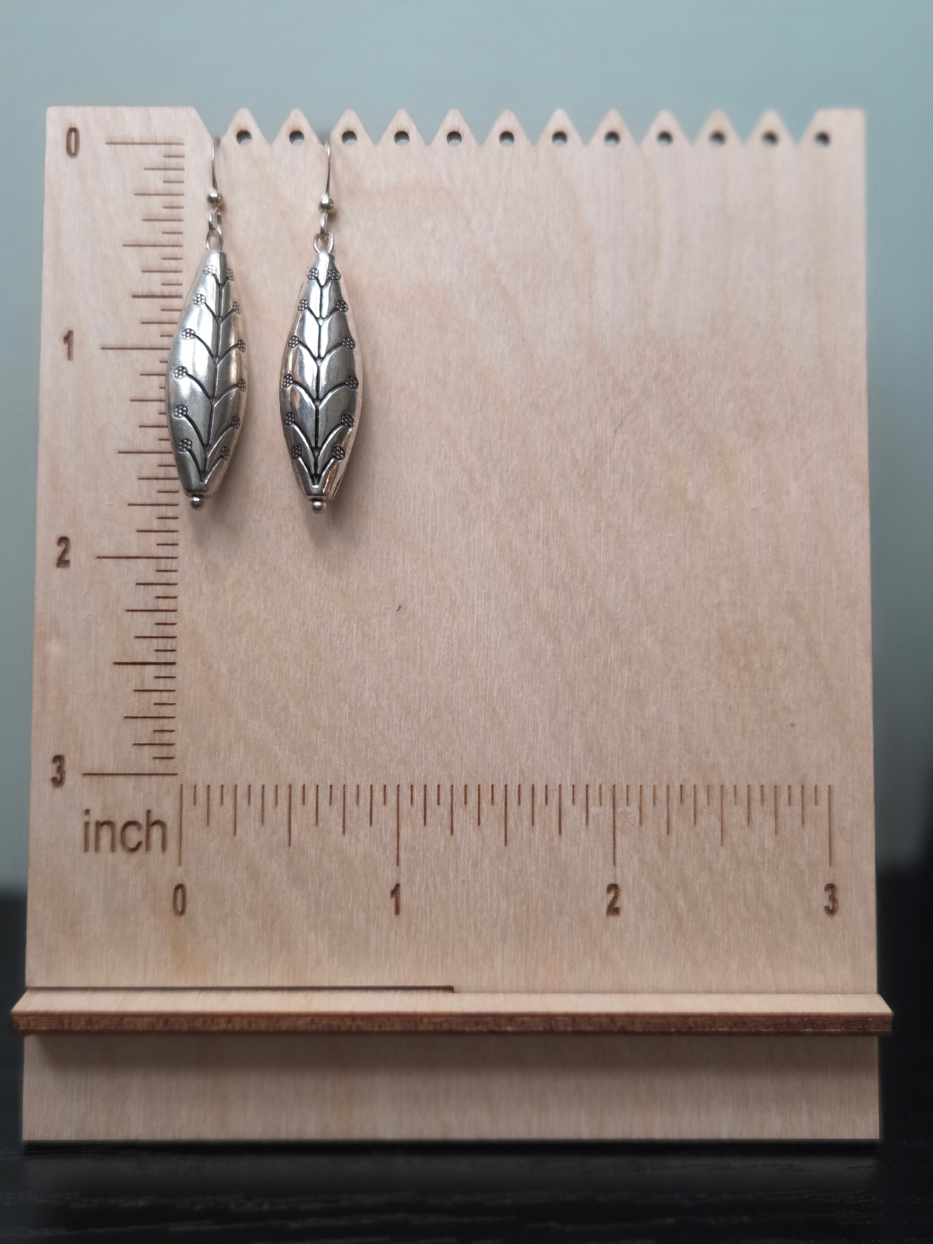 Pair of silver-tone etched leaf drop earrings shown against a woven burlap display card