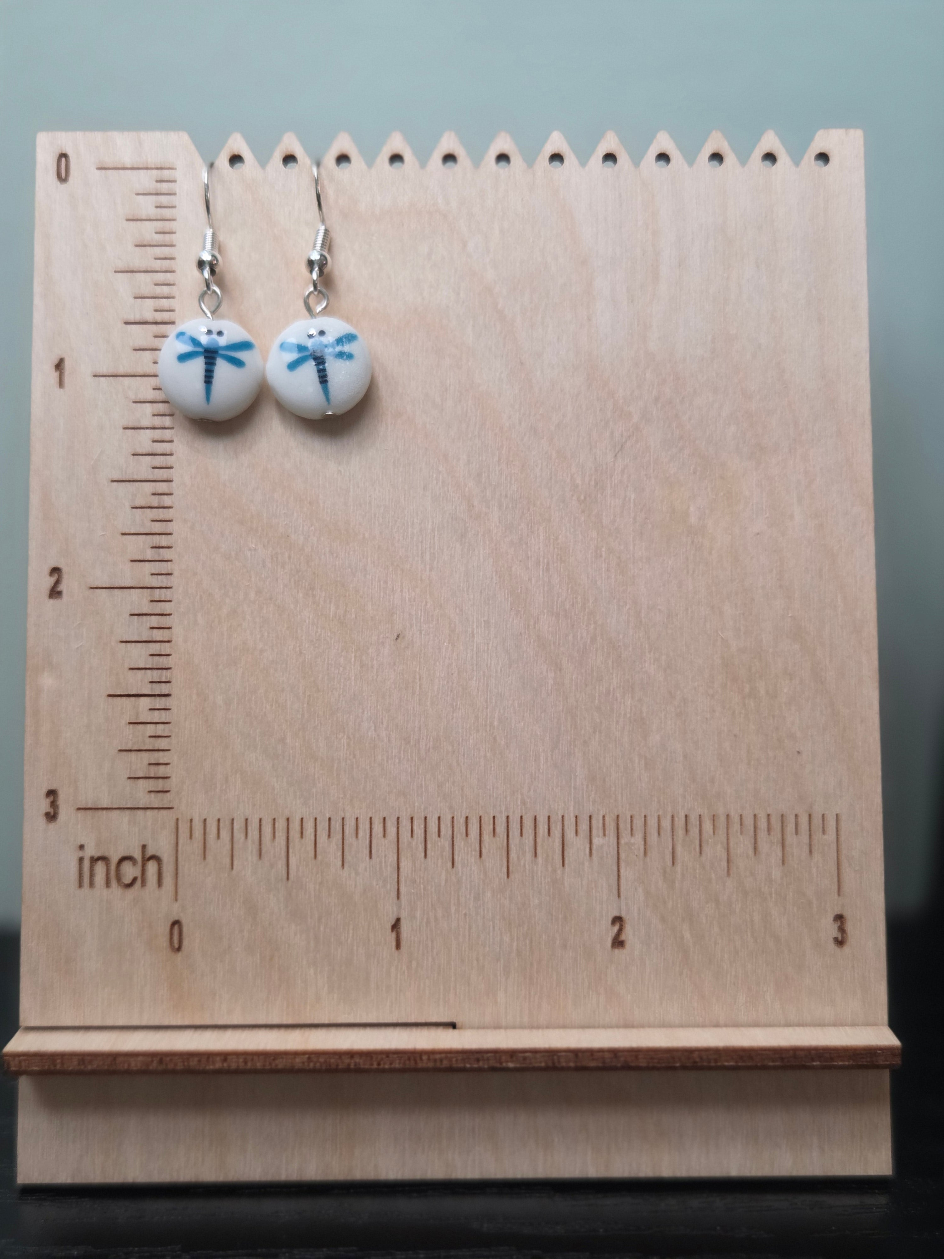 Close-up of painted blue dragonfly glass bead drop earrings shown against a wood block backdrop