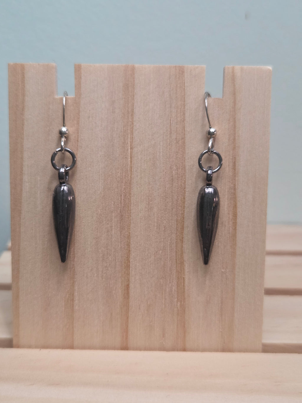 Gunmetal teardrop spike charm dangle earrings, shown on wood display