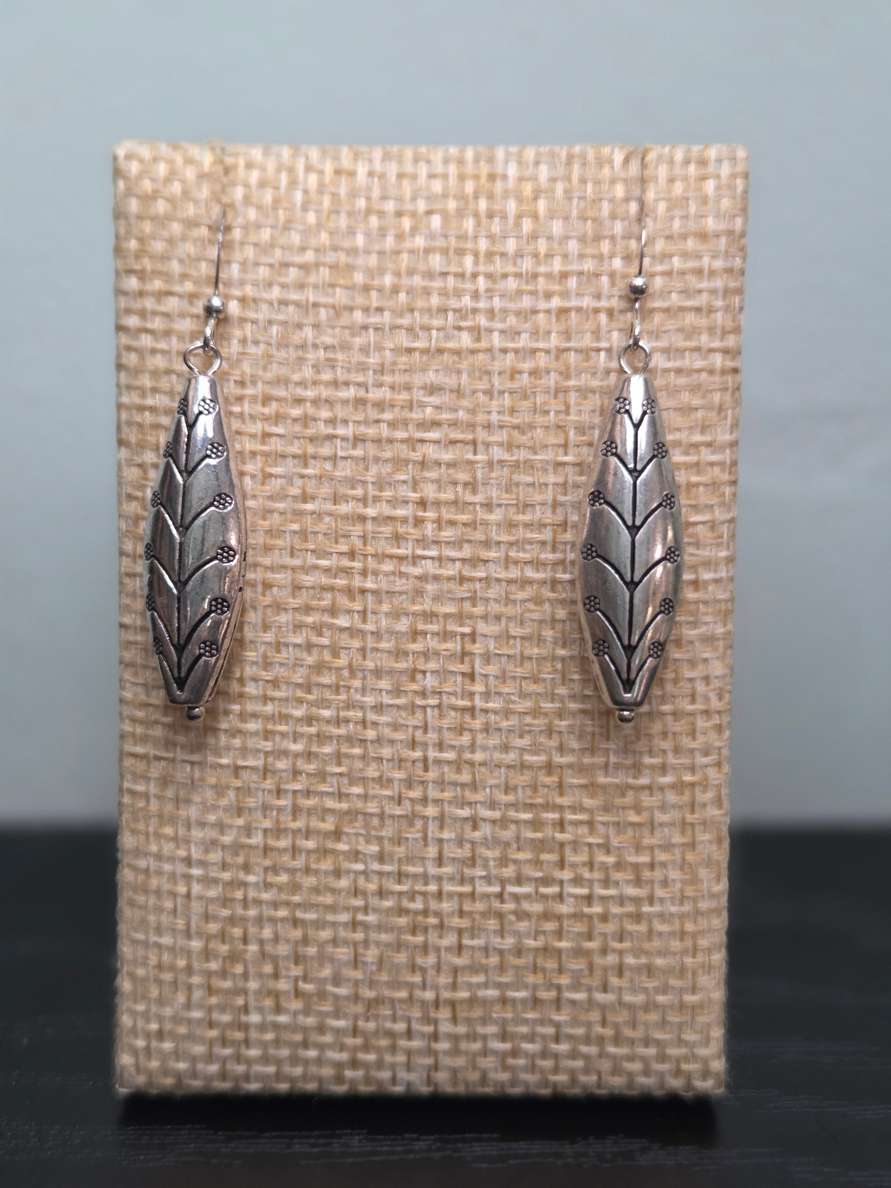 Pair of silver-tone marquise drop earrings with an etched leaf and floral design, shown on a wooden ruler stand measuring approximately 1.75 inches