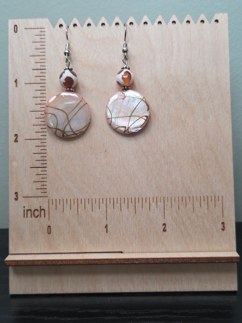 Close-up of iridescent crackle glass disc earrings with gold veining and mottled glass accent bead on woven fabric background