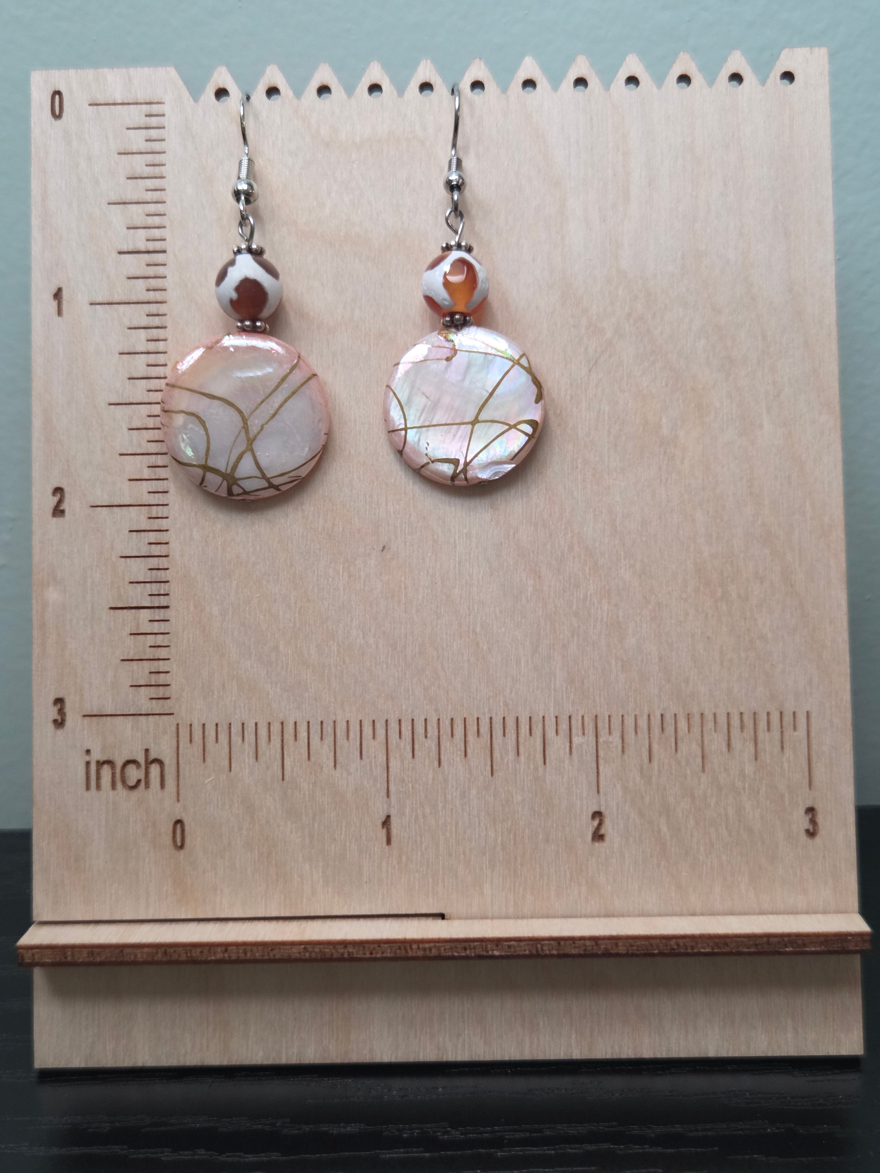 Close-up of iridescent crackle glass disc earrings with gold veining and mottled glass accent bead on woven fabric background