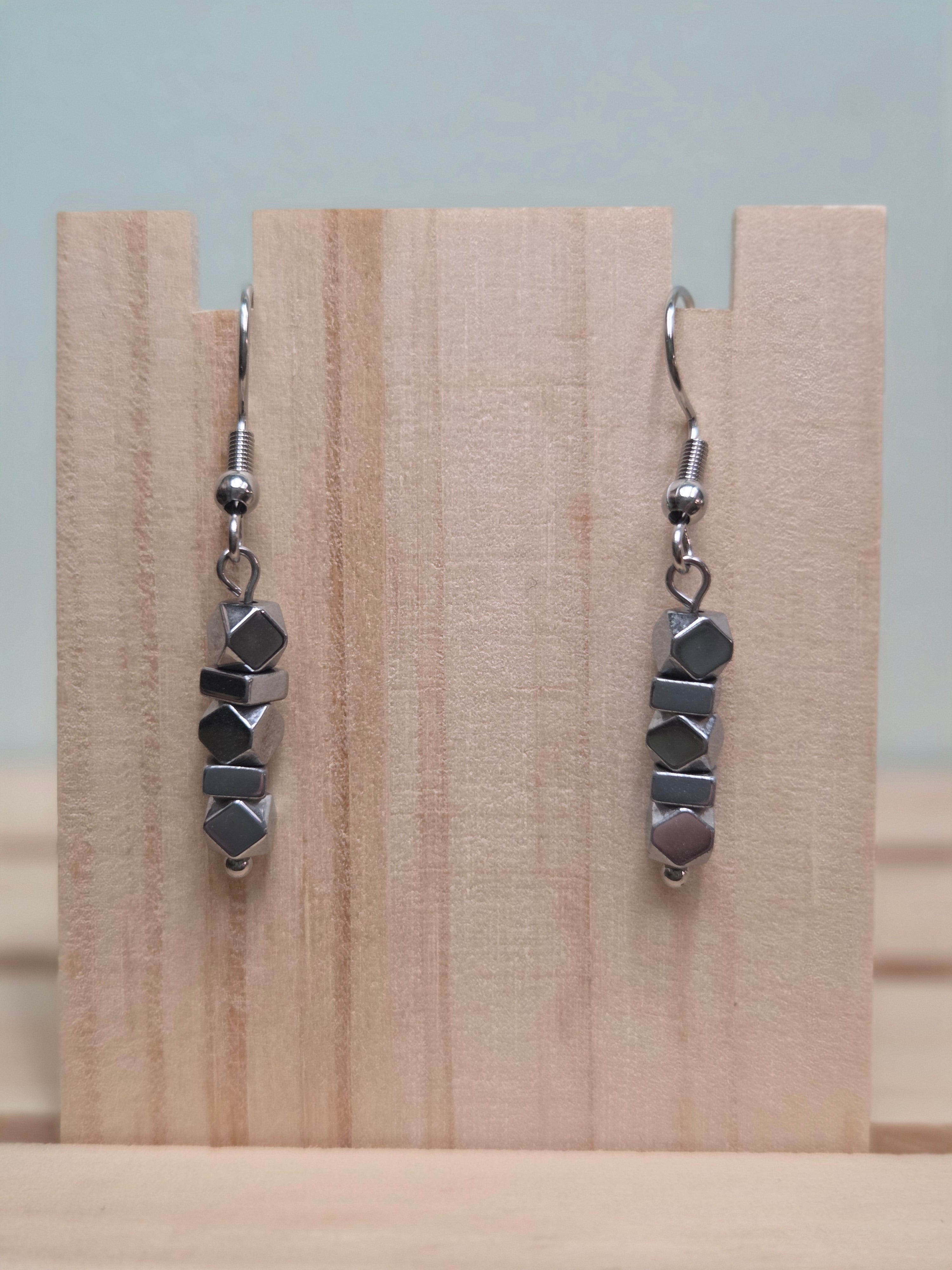 Pair of faceted hematite stack drop earrings shown on a wooden ruler stand measuring approximately 1.5 inches