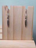 Gunmetal spike charm dangle earrings with faceted crystal accent, shown on wood display