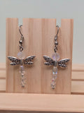 Crystal dragonfly drop earrings with antiqued silver-tone wings and iridescent AB crystal beads, shown on a wooden ruler stand measuring approximately 2 inches