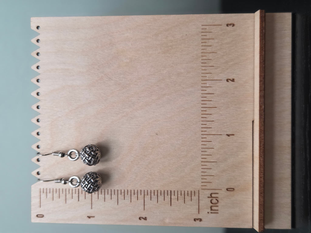 Close-up of silver-tone basketweave textured ball earrings hanging against a wood block backdrop