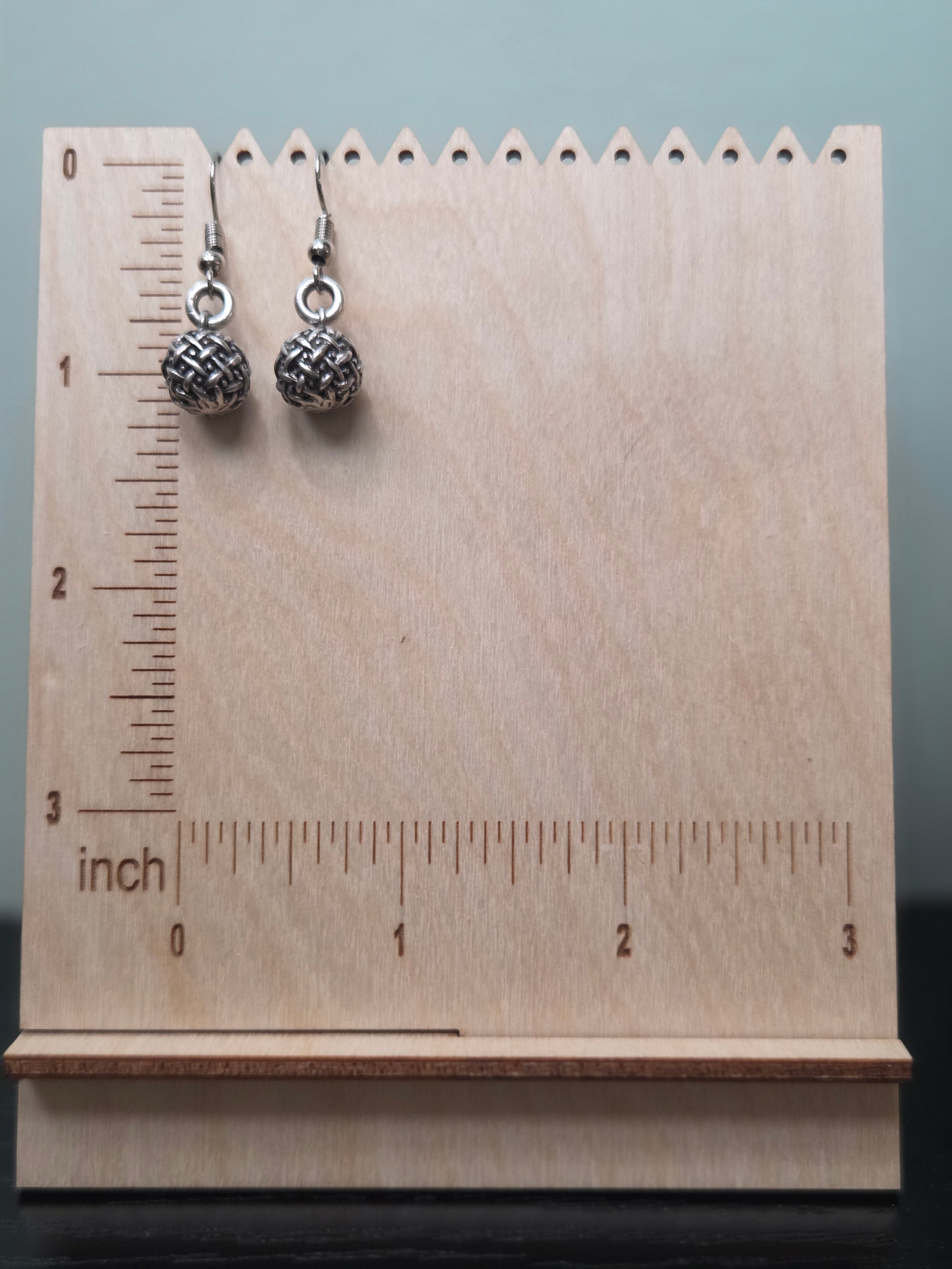 Close-up of silver-tone basketweave textured ball earrings hanging against a wood block backdrop