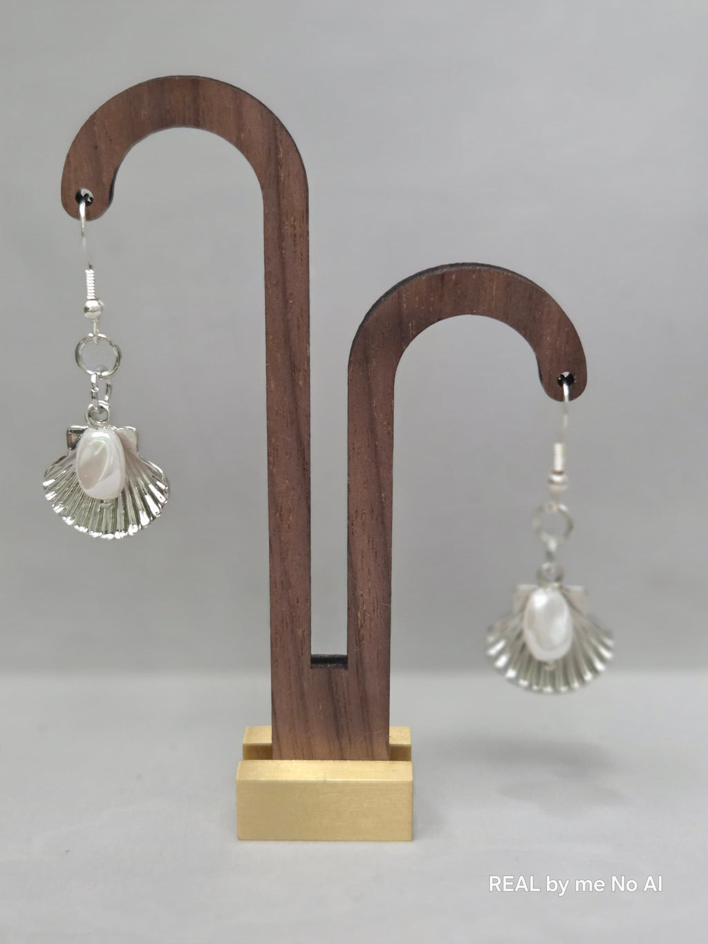 Silver-tone scallop shell earrings with a shell pearl center, on a plain background