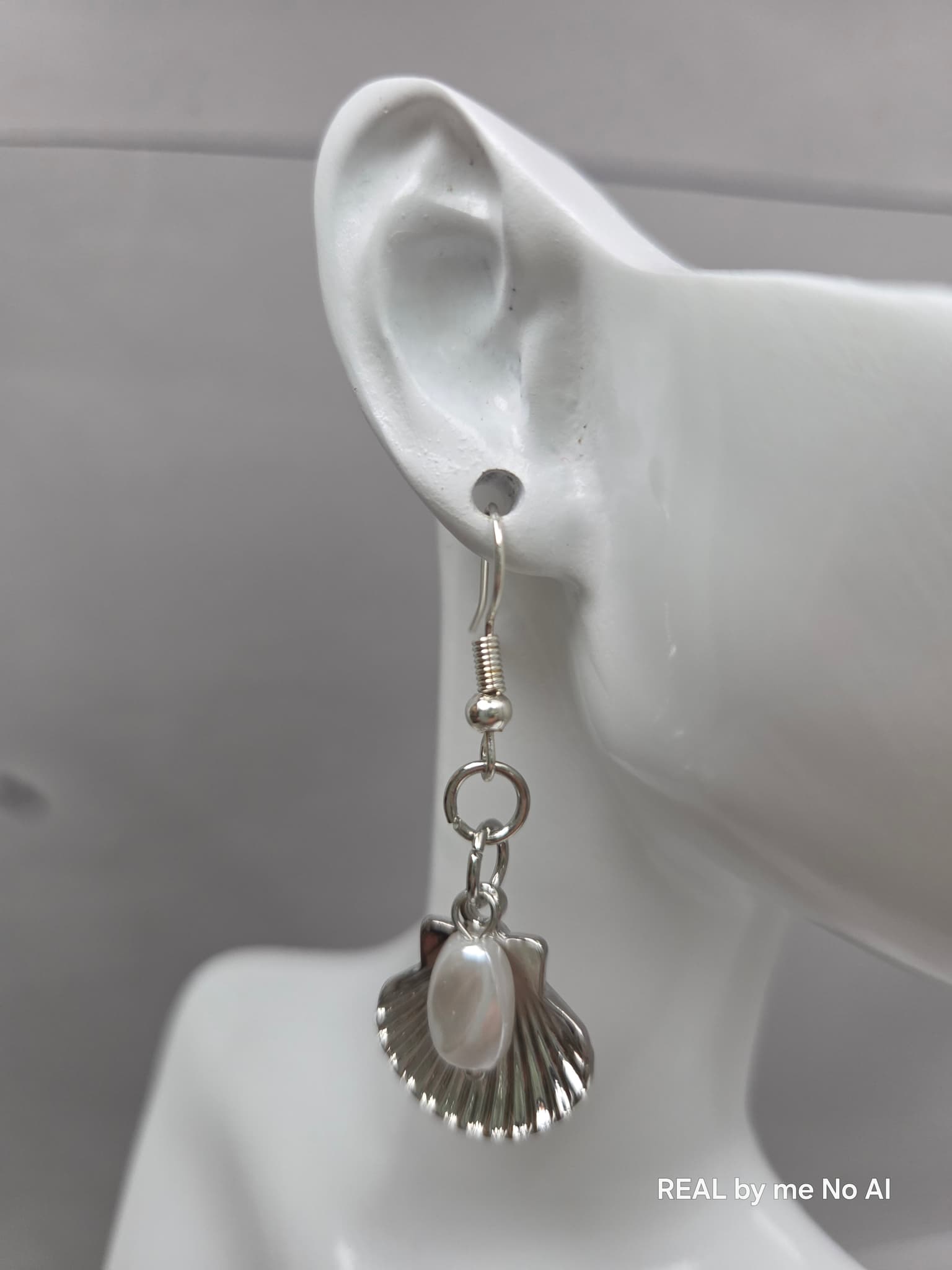 Pair of silver shell and pearl dangle earrings laid flat