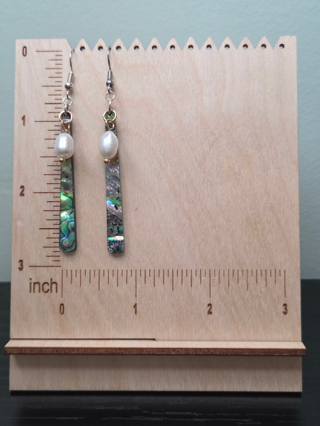 Freshwater pearl and abalone-style resin bar earrings displayed on a wooden earring stand with ruler showing approximately 2.75 inch length