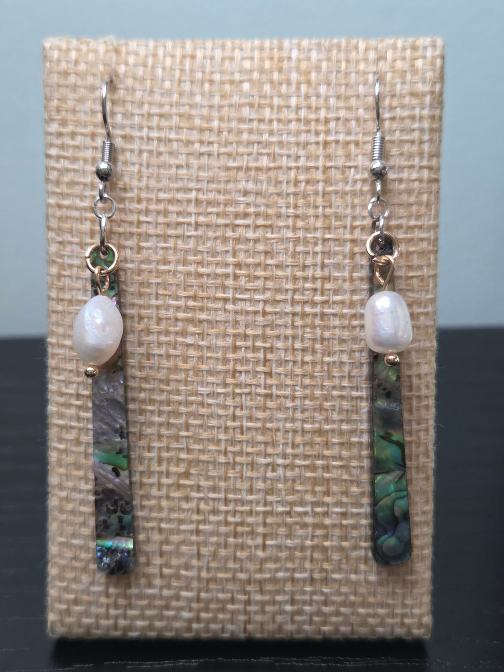 Freshwater pearl and abalone-style resin bar drop earrings with gold-tone findings, shown on a woven fabric background