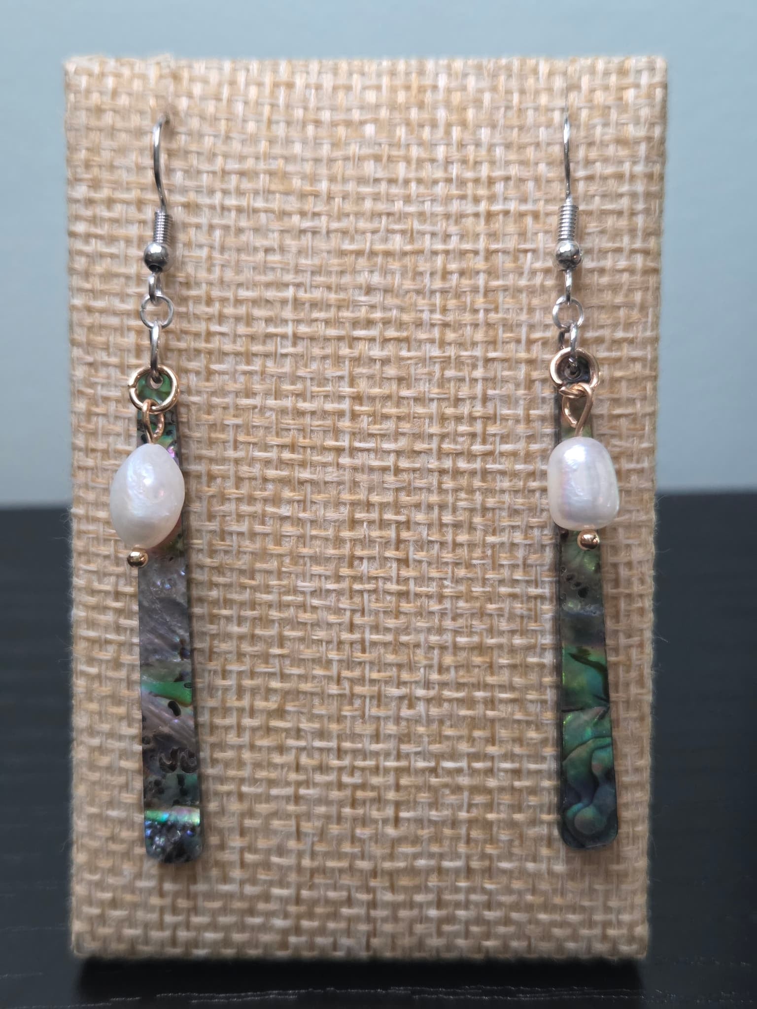 Freshwater pearl and abalone-style resin bar drop earrings with gold-tone findings, shown on a woven fabric background