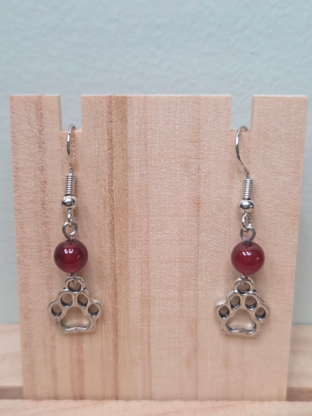 Paw print and mystery stone drop earrings displayed on a wooden earring stand with ruler showing approximately 1.5 inch length