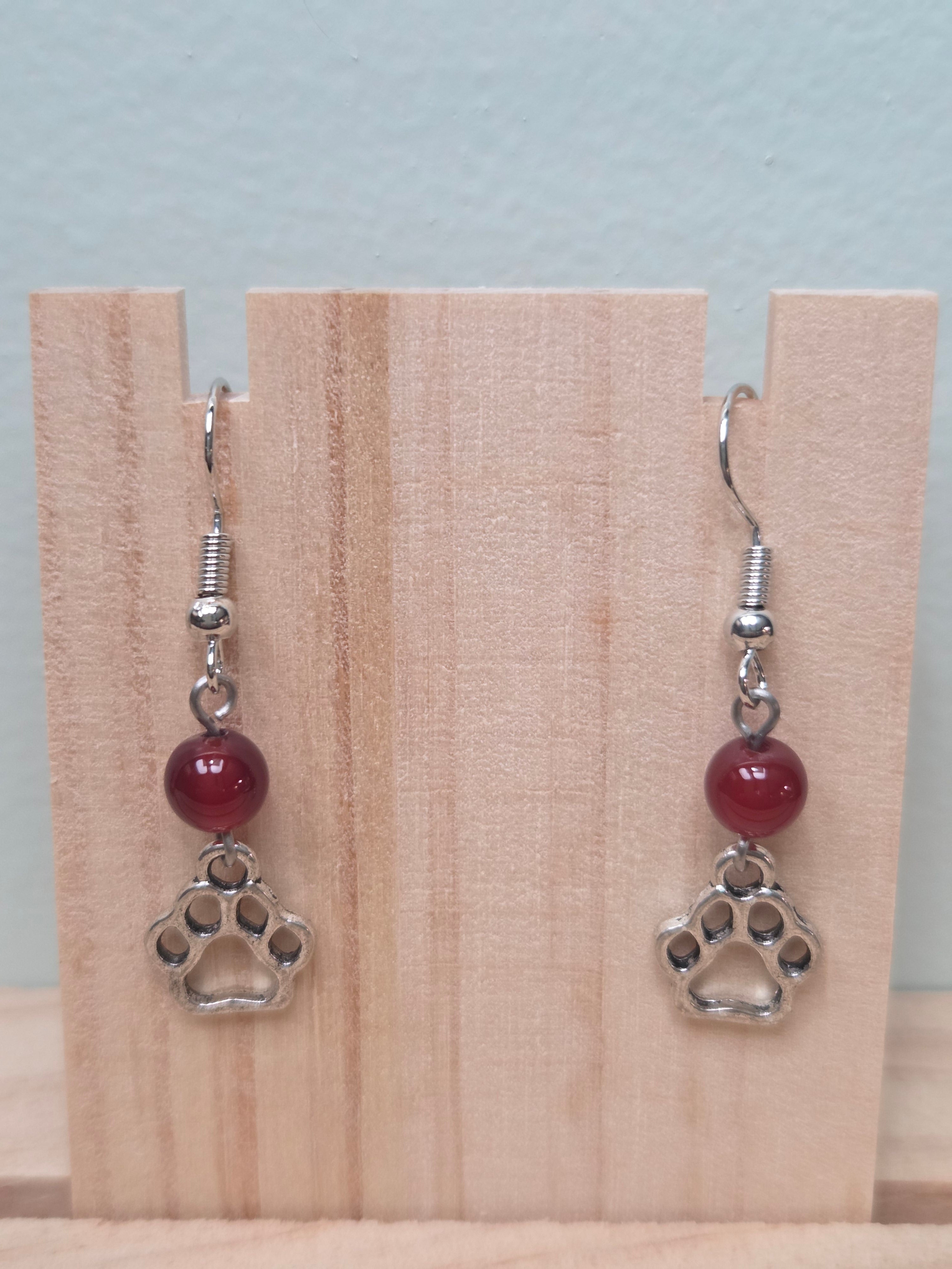 Paw print and mystery stone drop earrings displayed on a wooden earring stand with ruler showing approximately 1.5 inch length