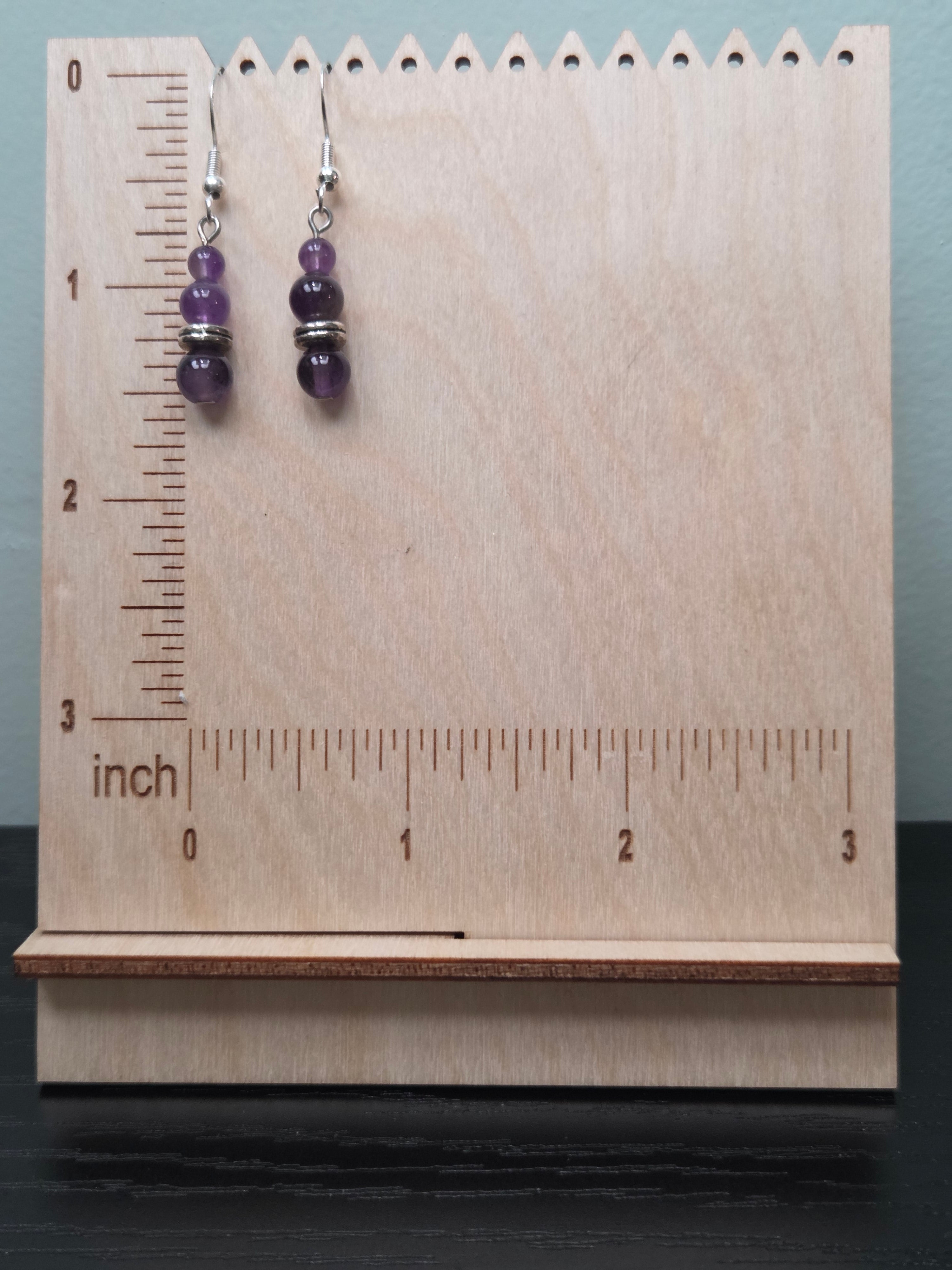 Close-up of stacked amethyst earrings showing graduated violet beads and silver-tone spacer on wood grain surface