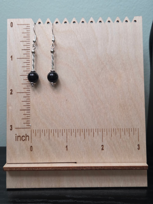 Close-up of black mystery stone earrings with twisted silver-tone tube accent on wood grain surface