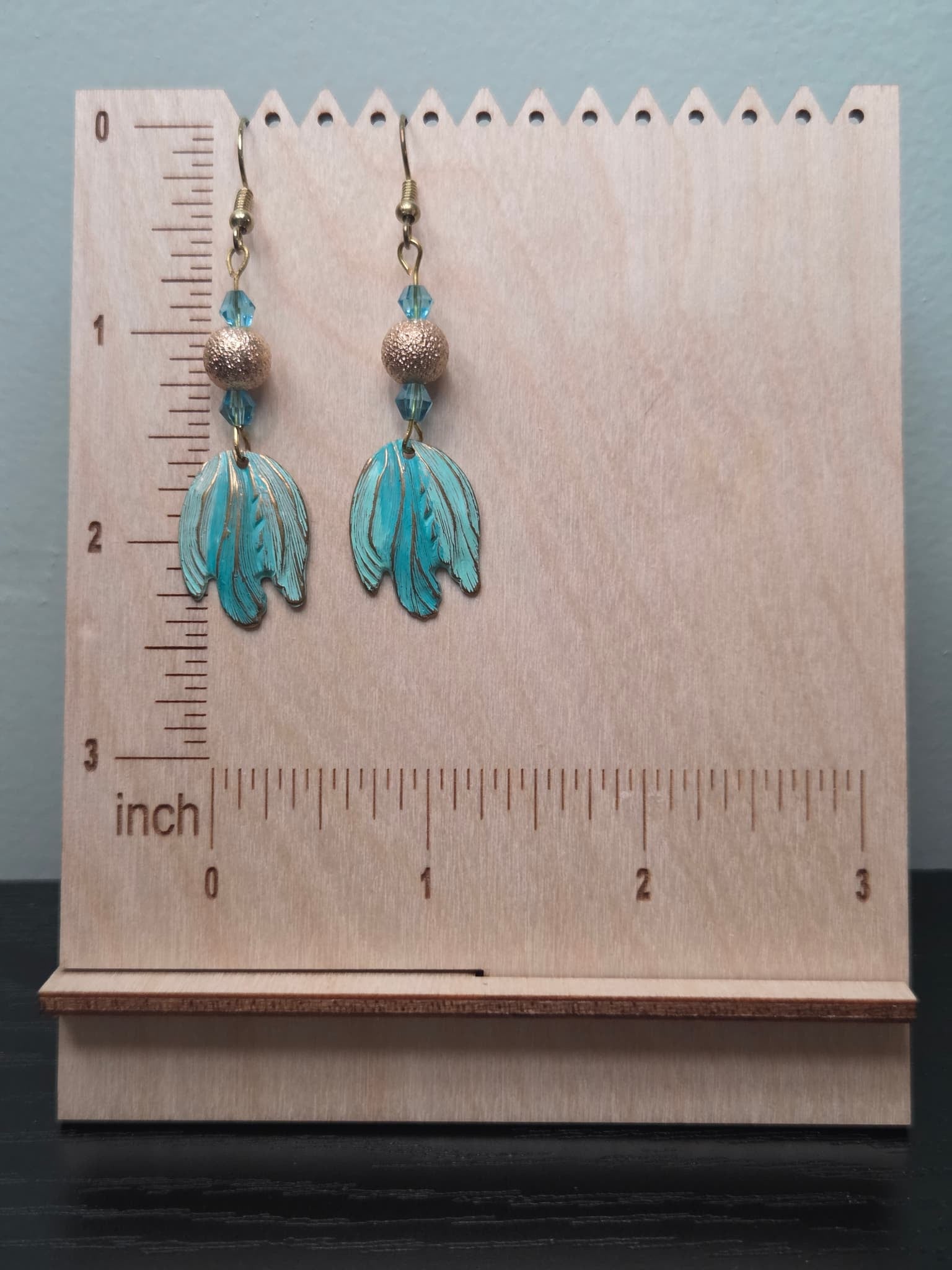 Turquoise and gold boho leaf earrings on wooden display stand with ruler showing approximately 2 inches in length