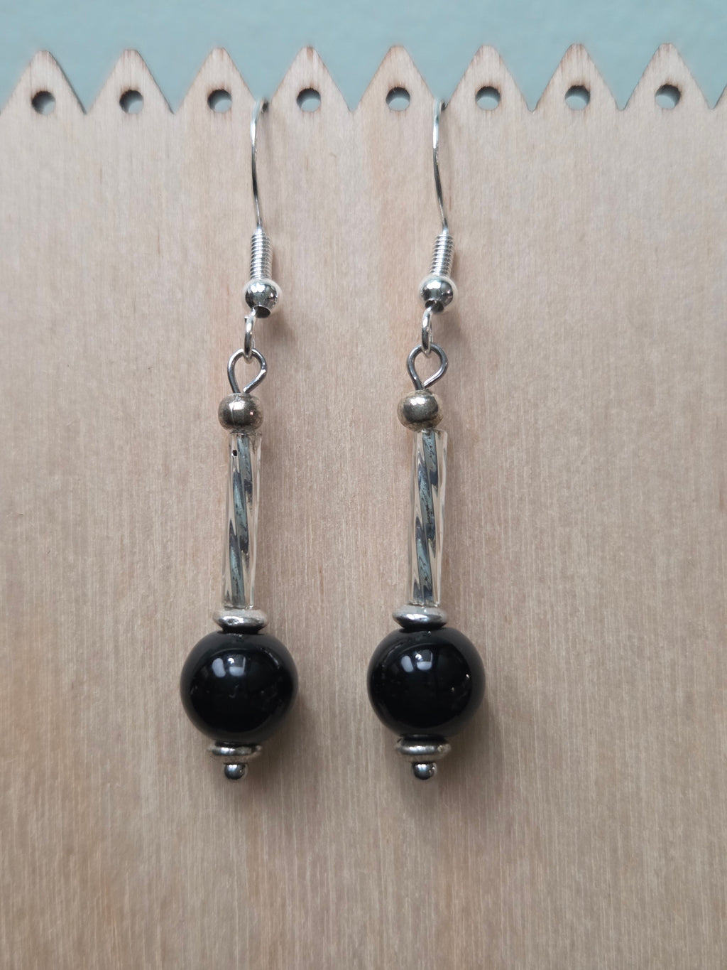 Black mystery stone drop earrings with twisted silver-tone tube, displayed on a wooden earring stand with ruler showing approximately 1.9 inch length