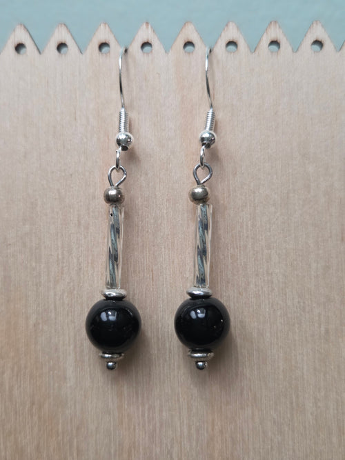 Black mystery stone drop earrings with twisted silver-tone tube, displayed on a wooden earring stand with ruler showing approximately 1.9 inch length