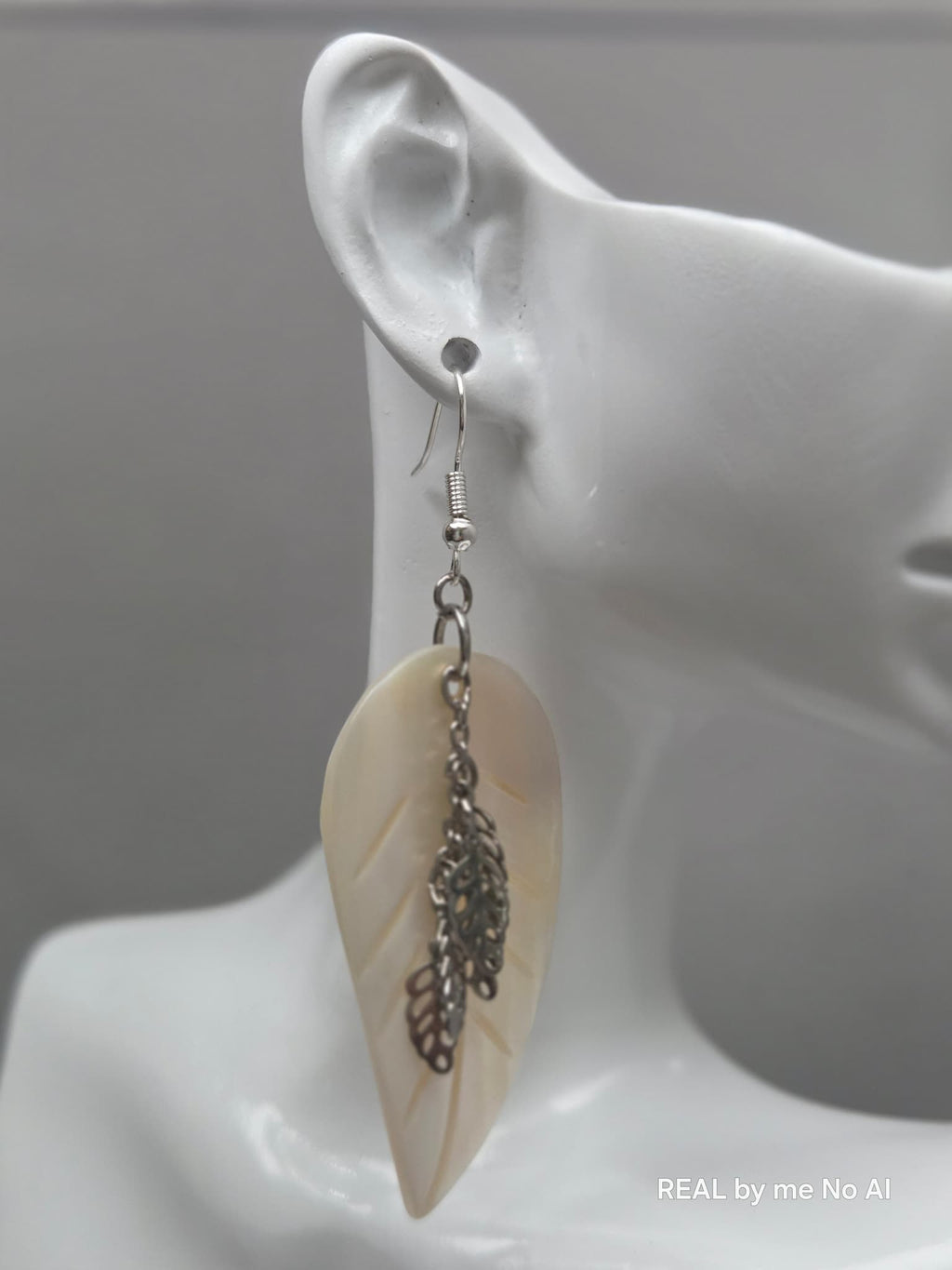 Pair of mother of pearl leaf earrings laid flat on a plain background