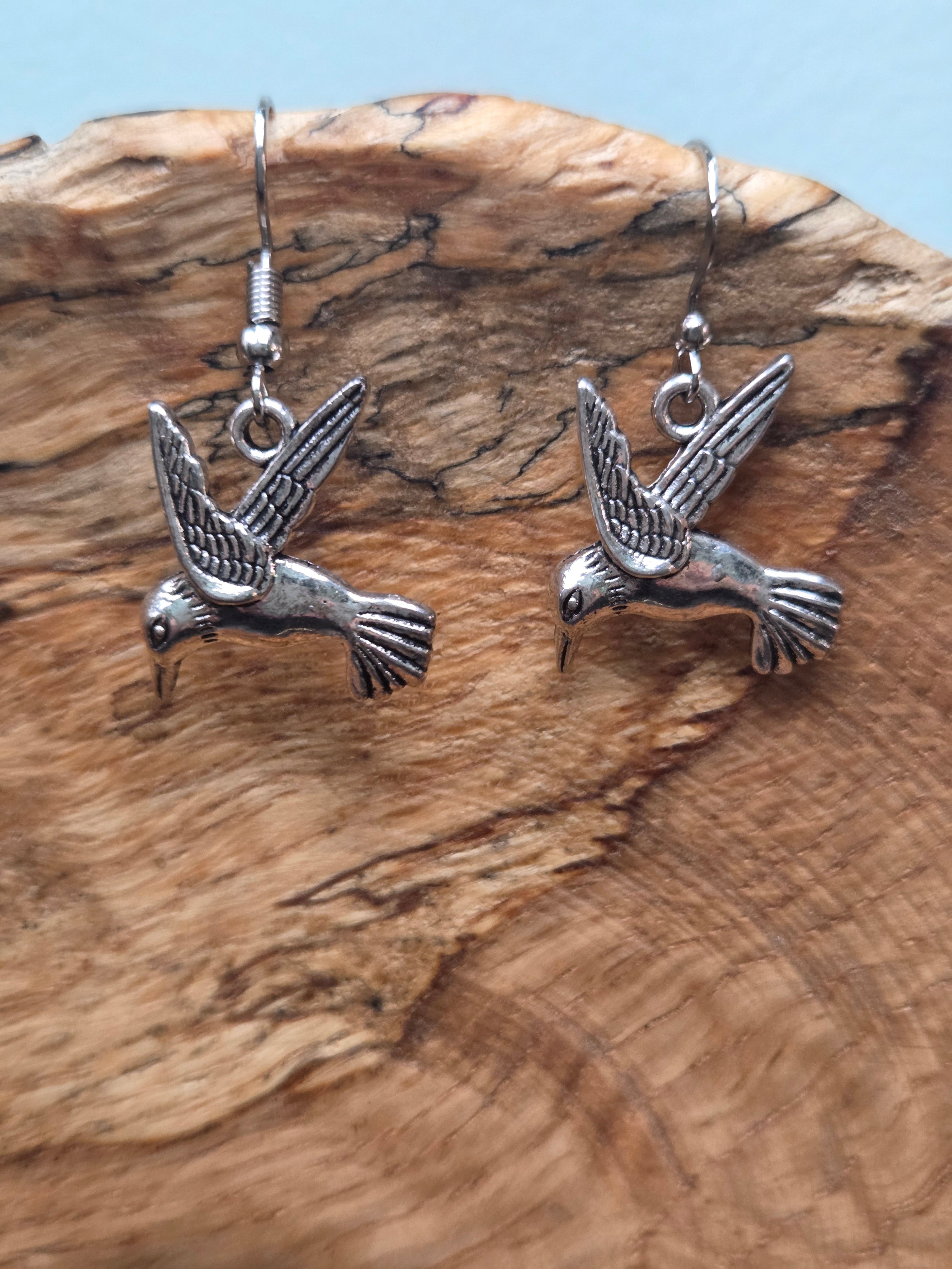 Silver-tone alloy hummingbird dangle earrings, diving bird design, shown on wood display