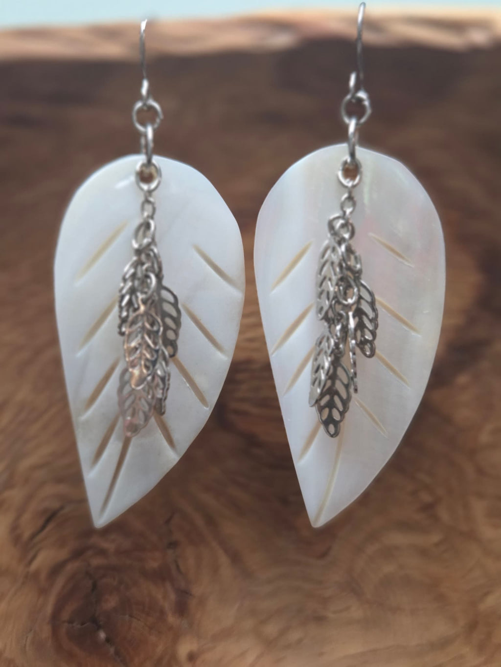 Alt Text (Image 1): Handmade mother of pearl carved leaf earrings with cascading silver filigree leaf charms, displayed on a wood surface