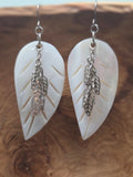Alt Text (Image 1): Handmade mother of pearl carved leaf earrings with cascading silver filigree leaf charms, displayed on a wood surface