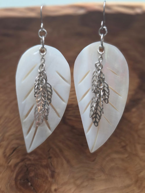 Alt Text (Image 1): Handmade mother of pearl carved leaf earrings with cascading silver filigree leaf charms, displayed on a wood surface