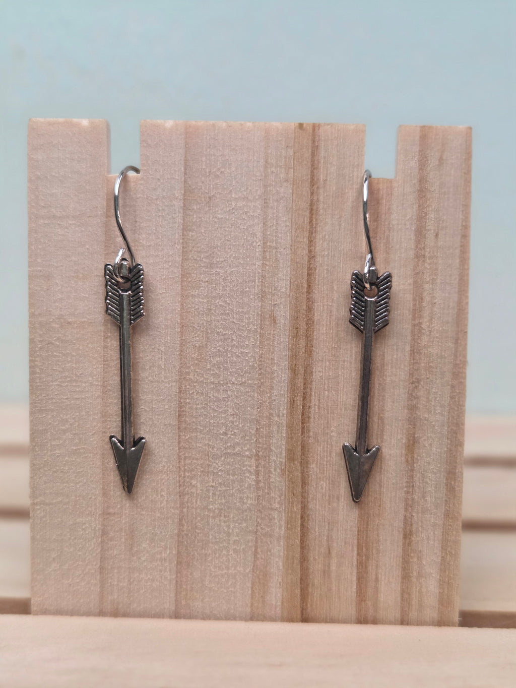 Gunmetal-tone arrow charm dangle earrings, shown on wood display