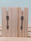 Gunmetal-tone arrow charm dangle earrings, shown on wood display