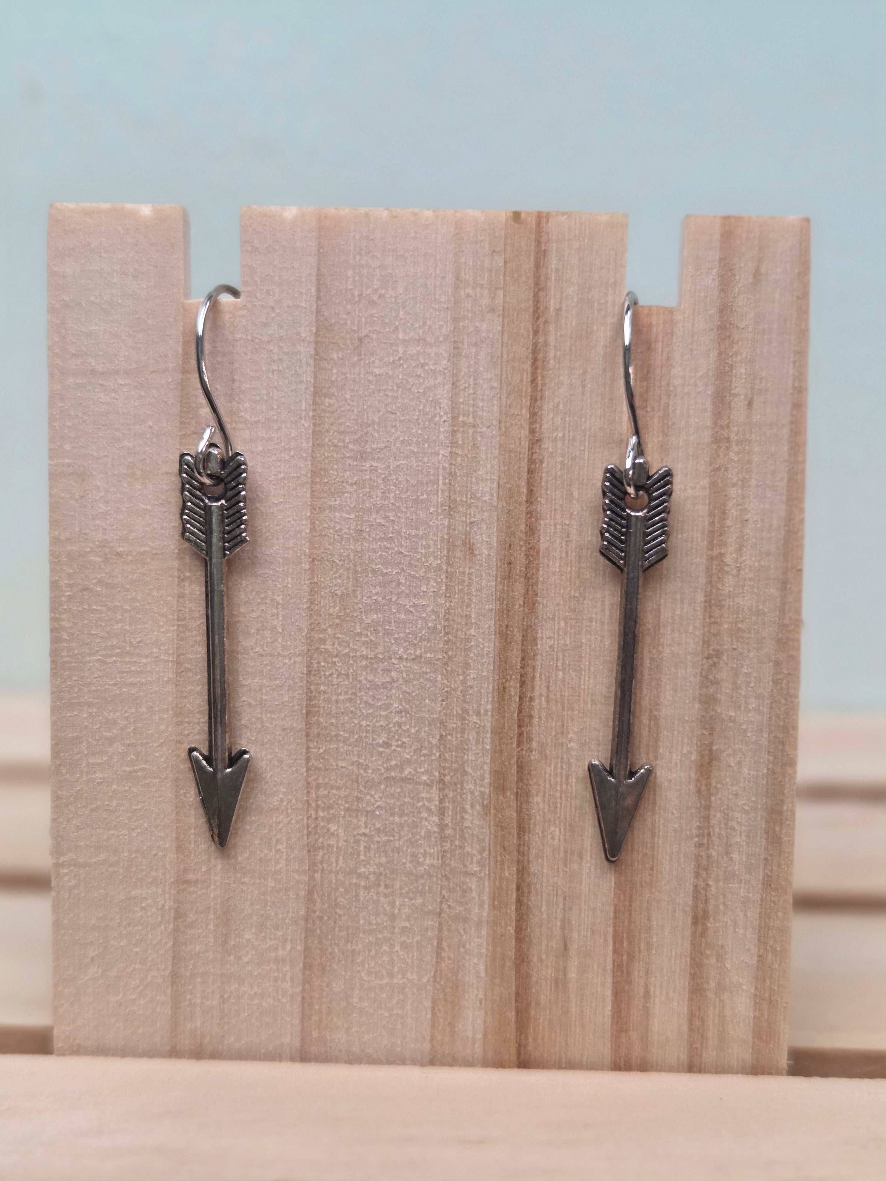 Gunmetal-tone arrow charm dangle earrings, shown on wood display