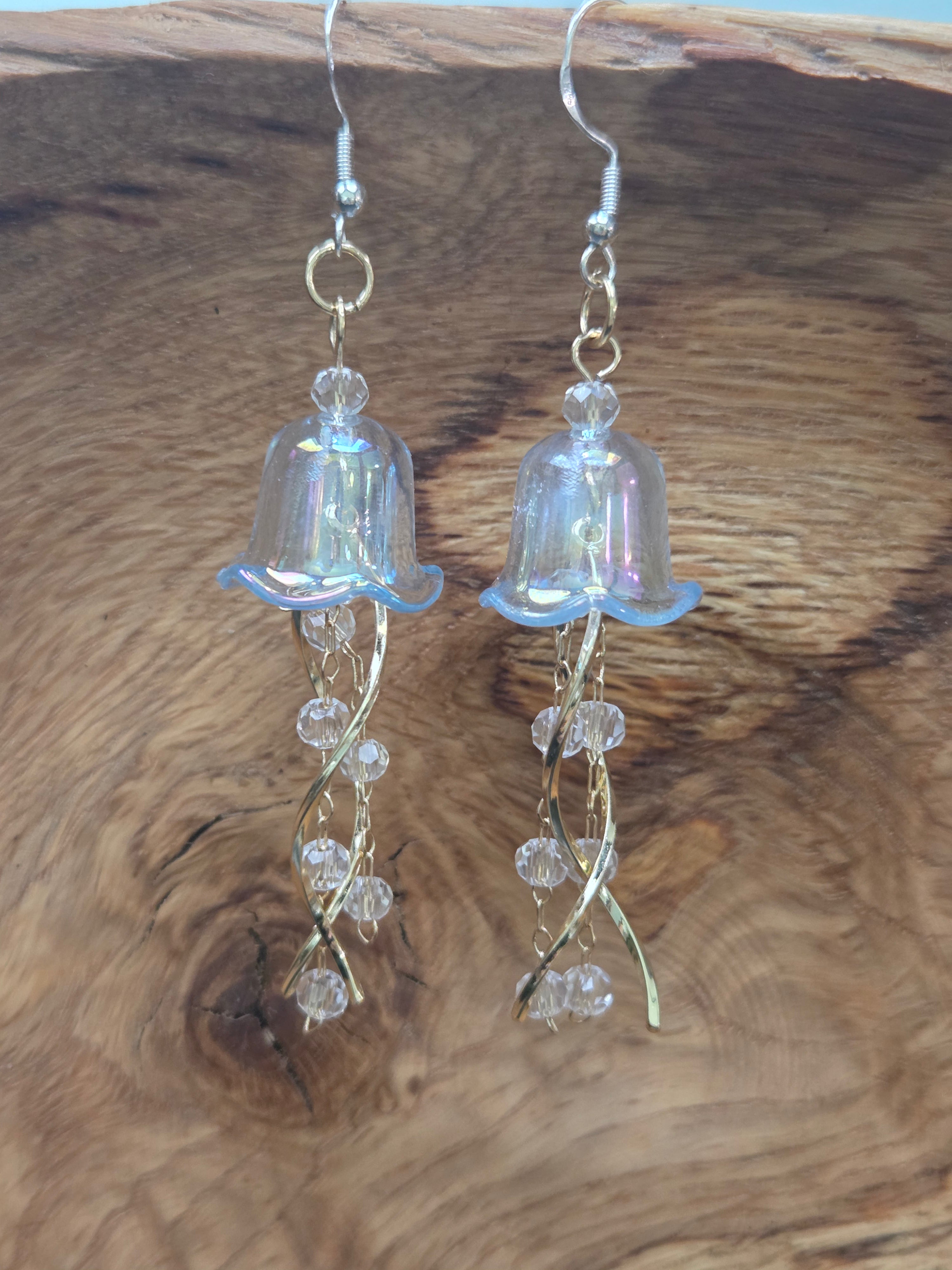 Close-up on natural wood, iridescent clear blue acrylic bell caps, gold-tone twisted wire tentacles, faceted crystal glass beads, silver fishhook ear wires