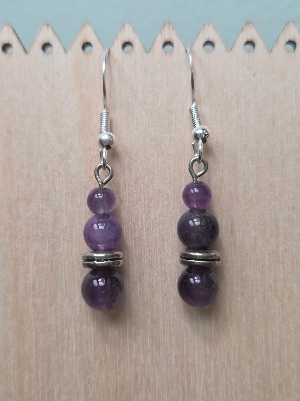 Stacked amethyst drop earrings with three graduated genuine amethyst beads and silver-tone disc spacer, displayed on a wooden earring stand with ruler showing approximately 1.5 inch length