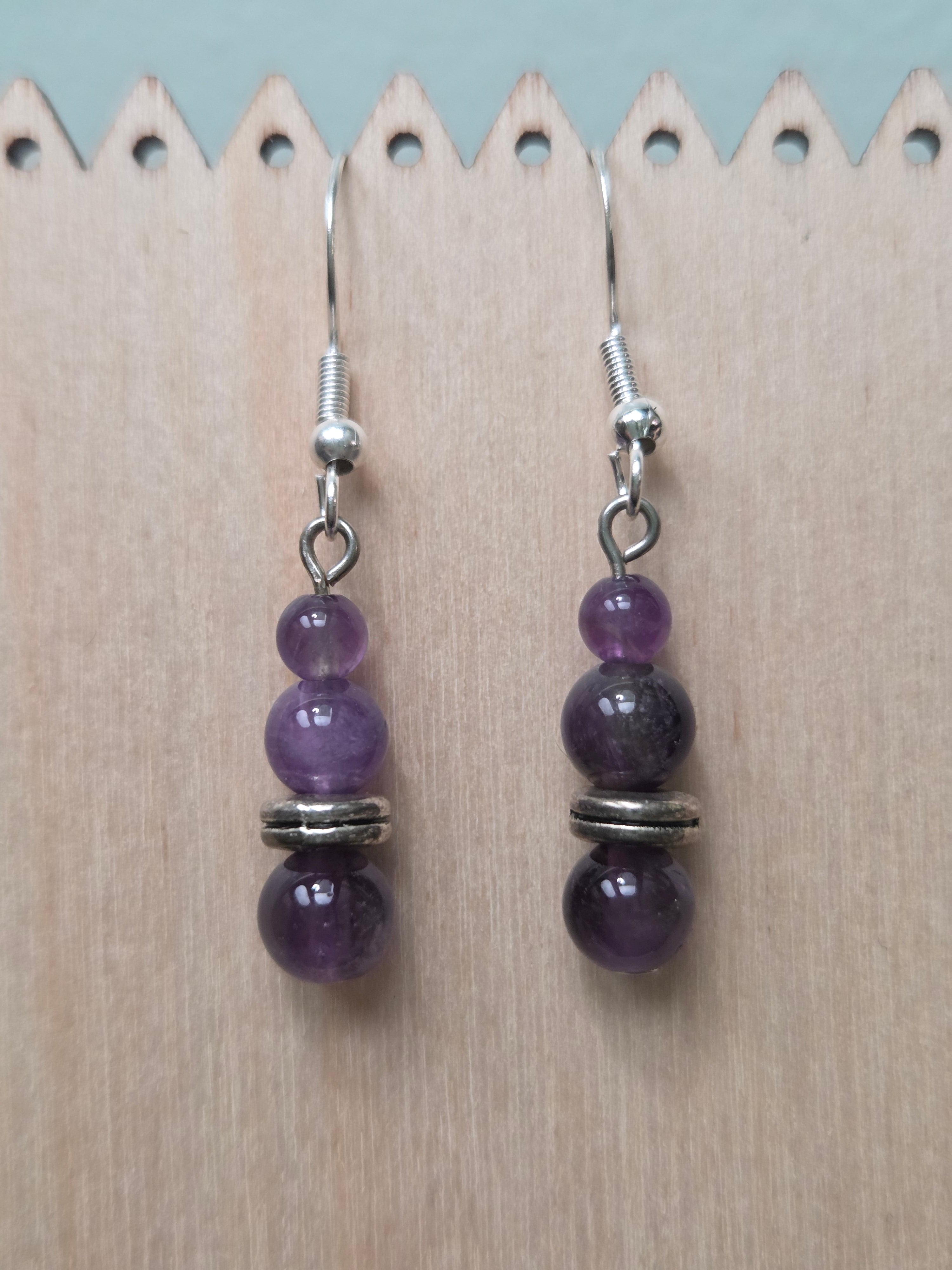 Stacked amethyst drop earrings with three graduated genuine amethyst beads and silver-tone disc spacer, displayed on a wooden earring stand with ruler showing approximately 1.5 inch length