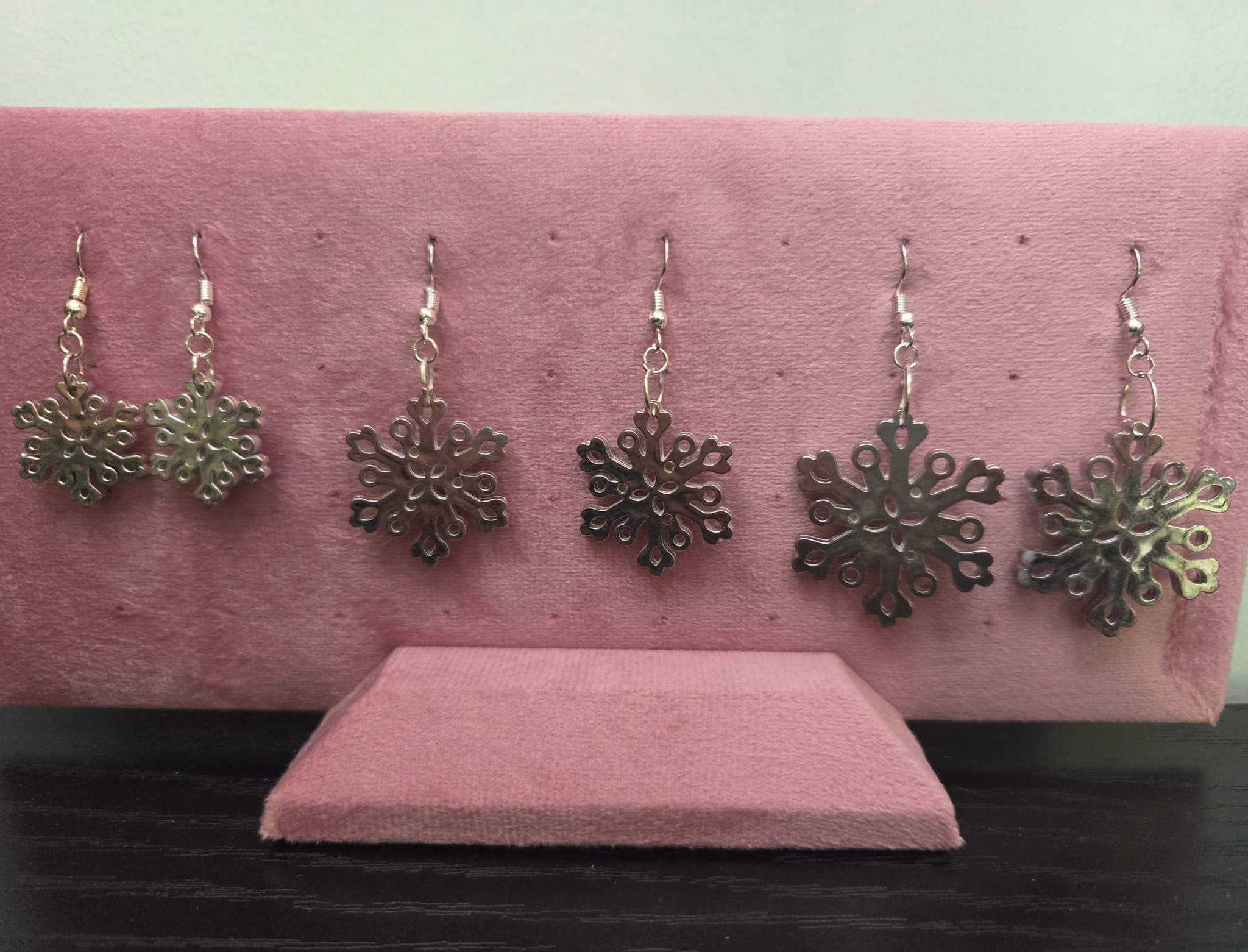 Lineup of acrylic snowflake earrings in three sizes, small, medium, and large, displayed on a pink jewelry holder