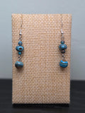 Pair of mystery stone graduated drop earrings with swirled turquoise, black, and tan beads, shown against a woven burlap display card