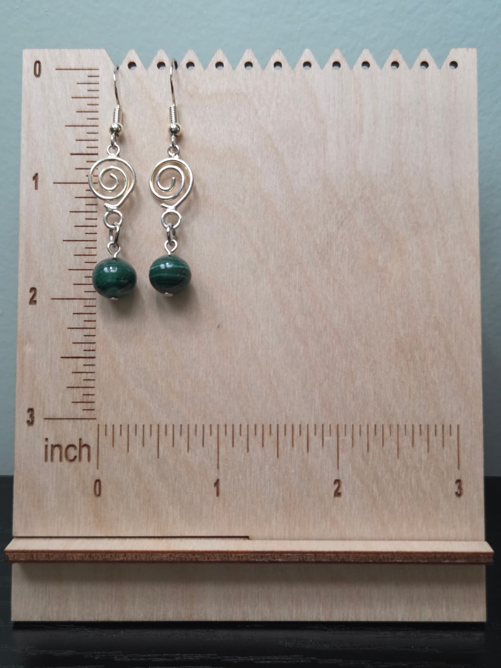 Close-up of genuine malachite bead earrings with silver-tone spiral charm on a woven fabric background