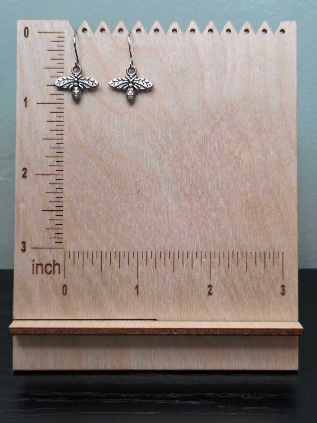 Silver-tone bee charm dangle earrings against ruler showing approximately 1 inch length