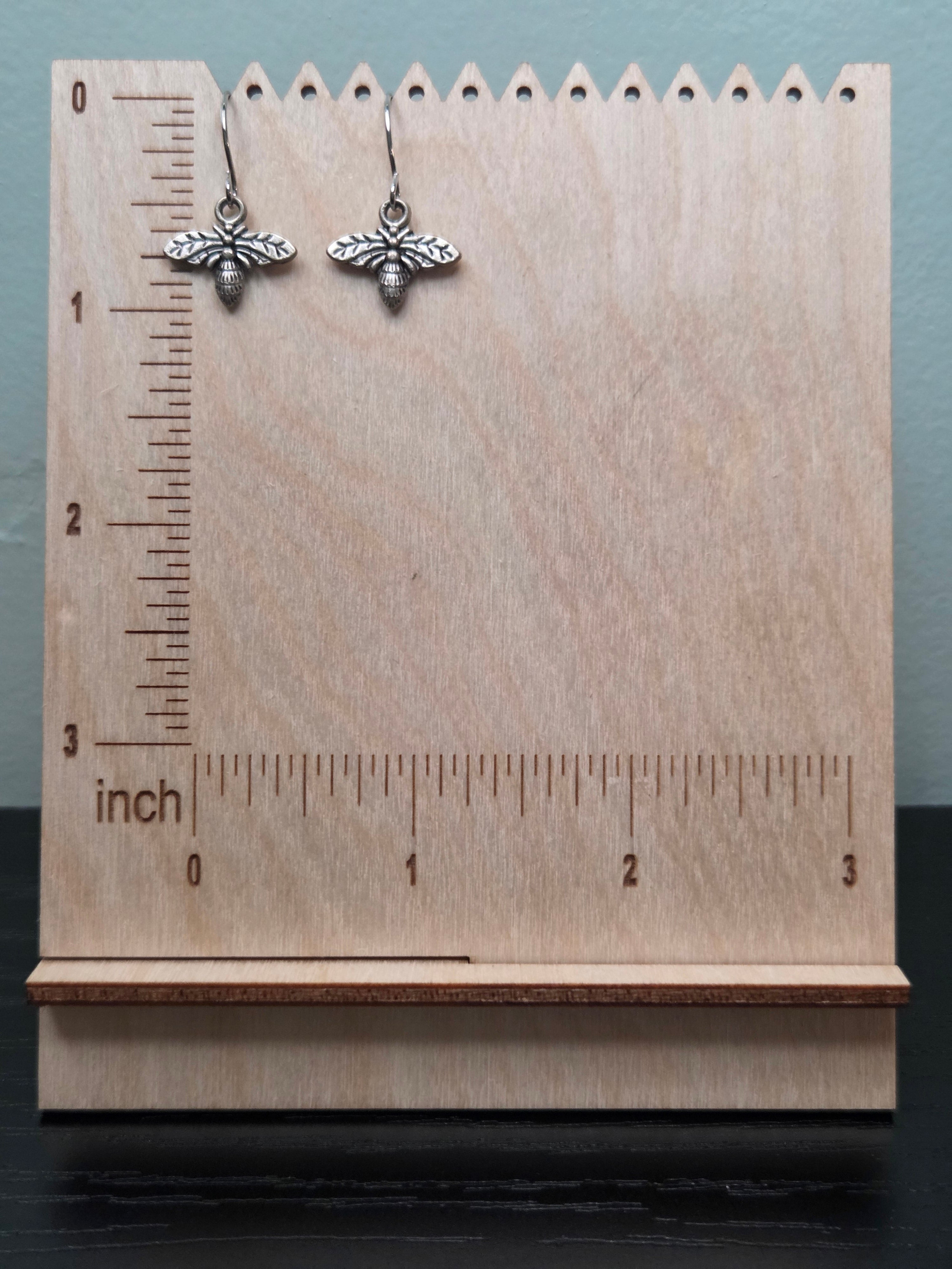 Silver-tone bee charm dangle earrings against ruler showing approximately 1 inch length